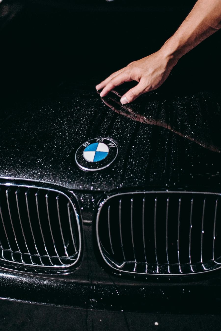Water beading on a freshly coated black hood as a hand glides across it