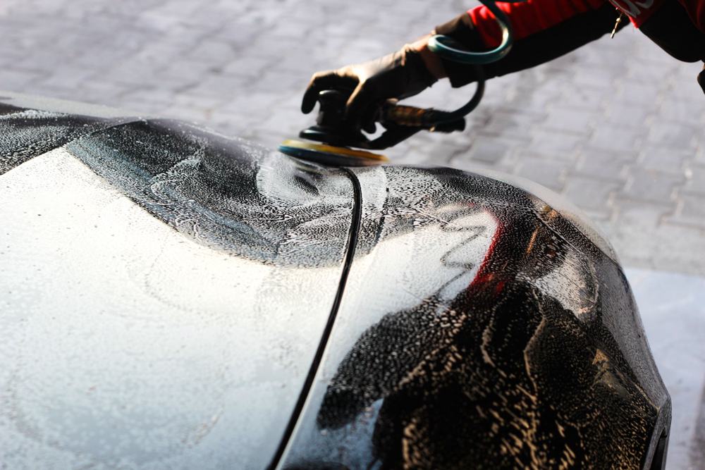 Polisher working through a wet black hood during paint correction