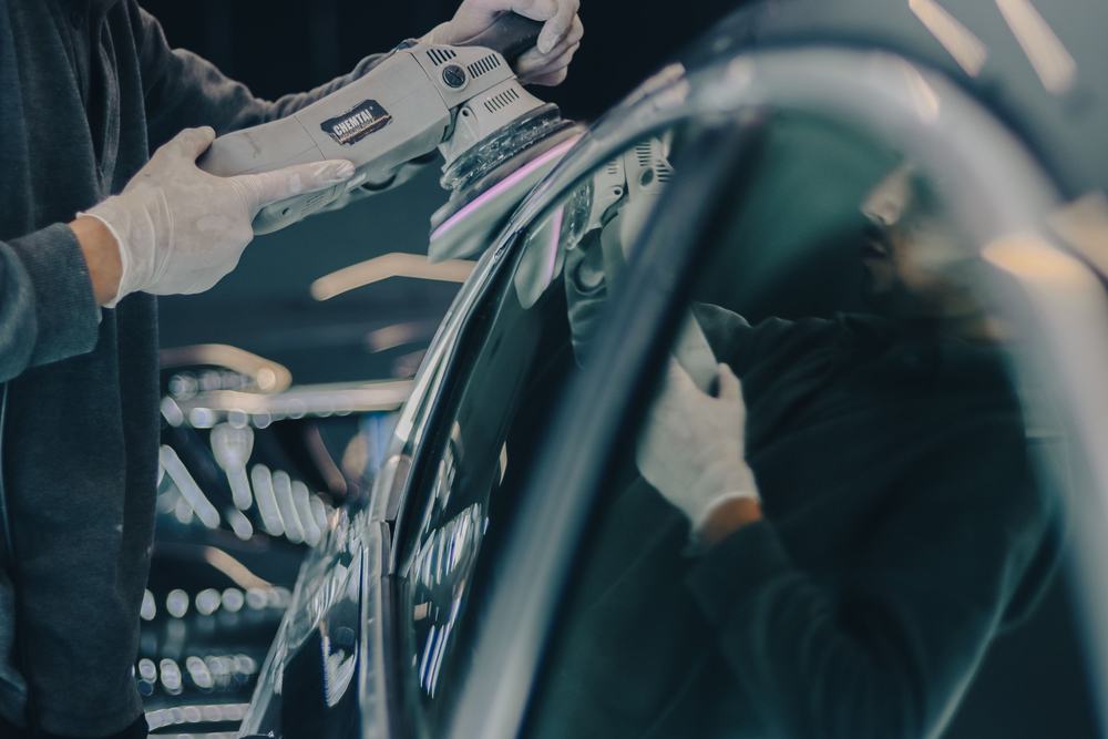 Detailer in gloves polishing a dark car's paint with a dual-action polisher