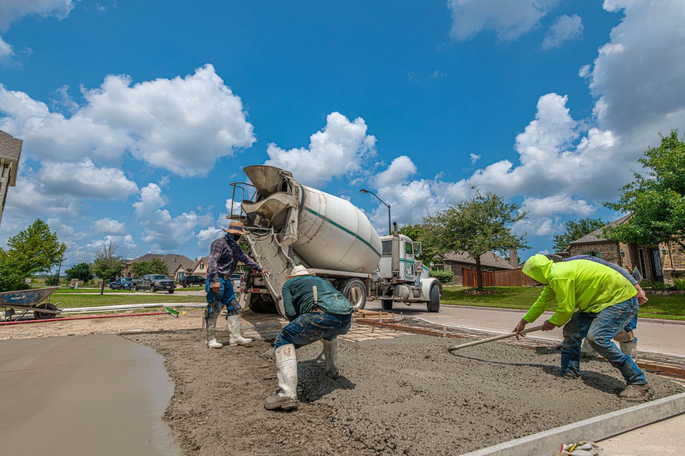 Crew pouring and raking concrete from a mixer truck for a new driveway