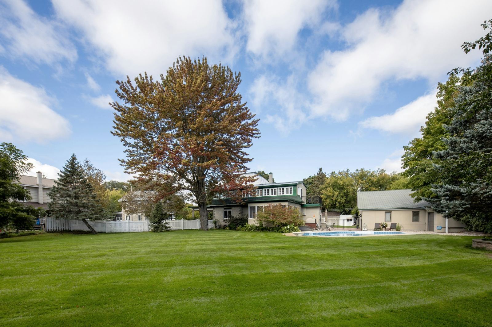 Freshly striped lawn behind a two-story home with a pool and a big shade tree