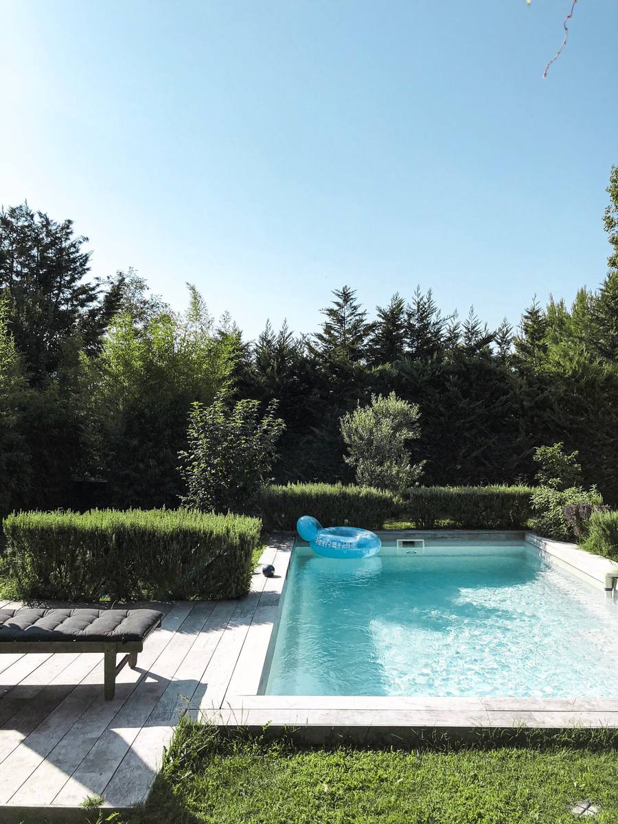 Clear turquoise backyard pool with a float, a lounge chair and a tall hedge