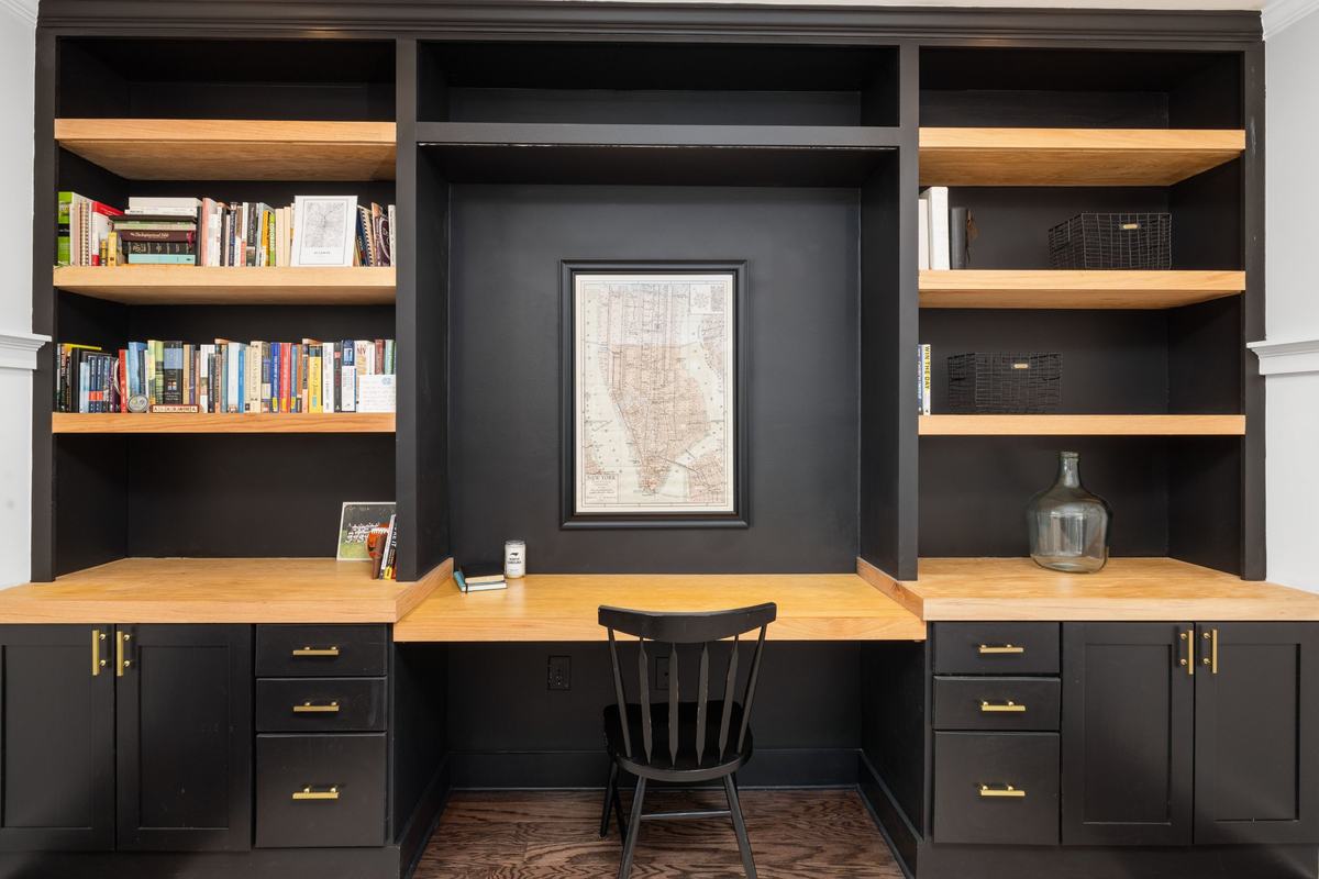 Built-in desk wall with black cabinets, brass pulls and oak shelves