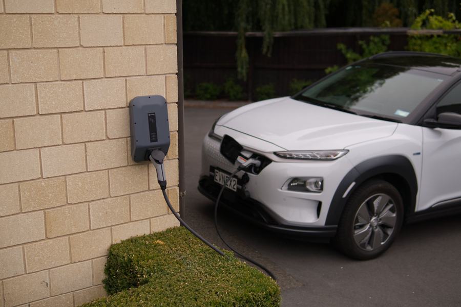 Wall-mounted EV charger plugged into an electric SUV in the driveway