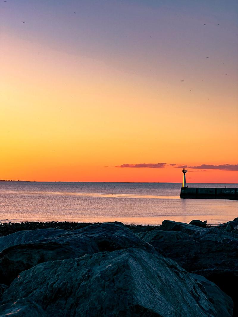 Sun going down behind the jetty light, rocks in the foreground